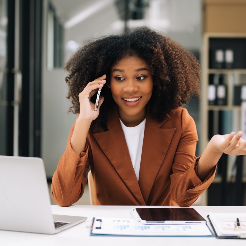 Profissional sorrindo ao telefone em mesa de trabalho com relatórios impressos e tablet