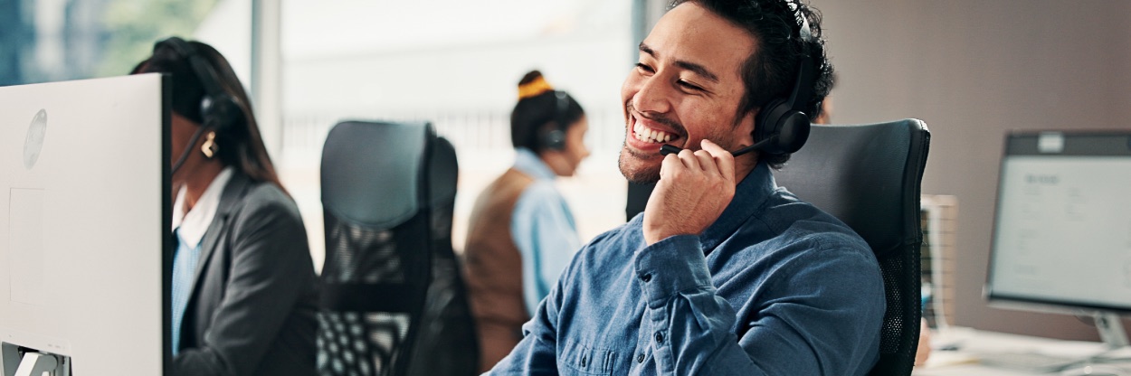 Equipe de atendimento com headset em central, com um atendente sorrindo em primeiro plano